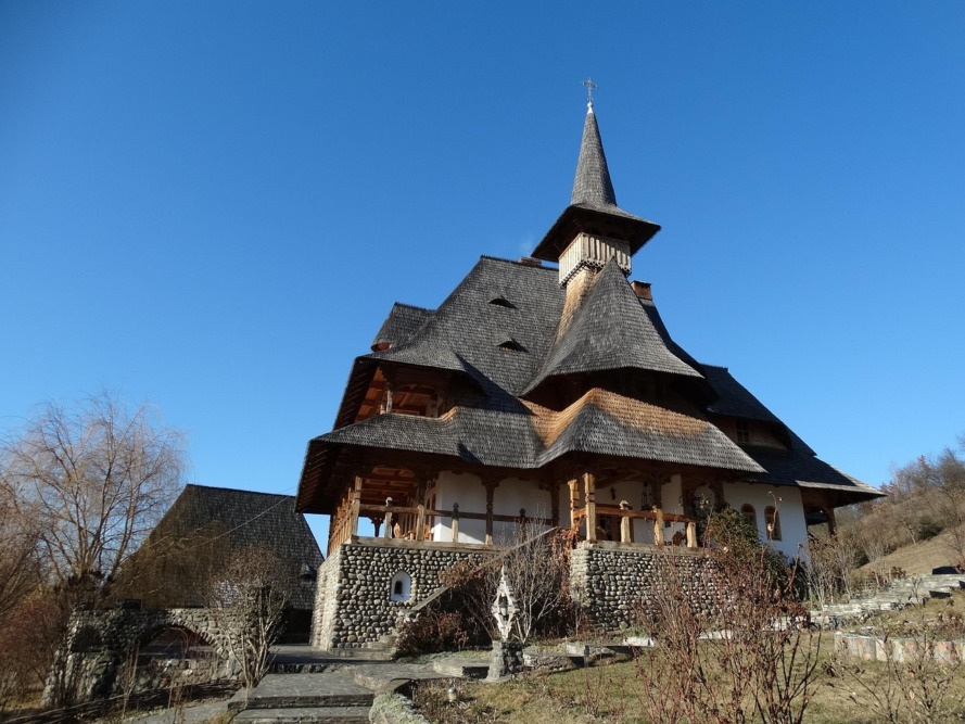 Iglesia de madera tradicional rumana en Maramureș, con tejado de tablillas y escalonado bajo cielo azul.