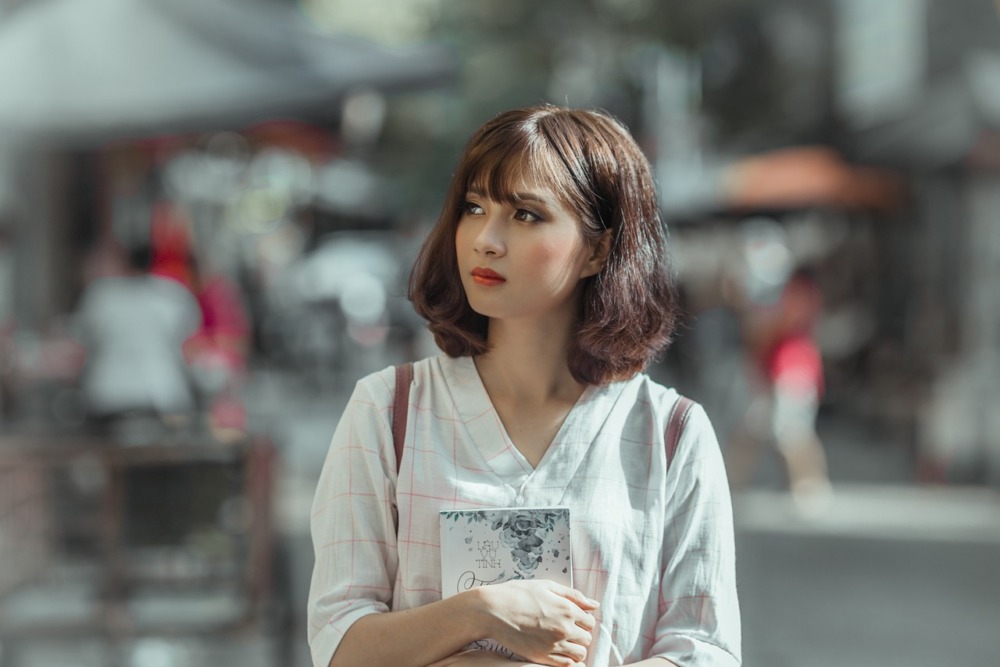 chica asiática con un libro entre sus manos observando la ciudad 