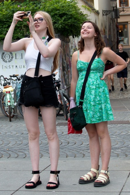 dos chicas con outfits de verano  en el centro de una ciudad realizando una fotografía y disfrutando