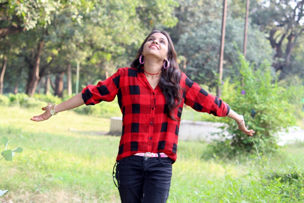 chica con los brazos abiertos, una camisa de cuadros rojos y negros y un vaquero negro, disfrutando del aire libre en el campo